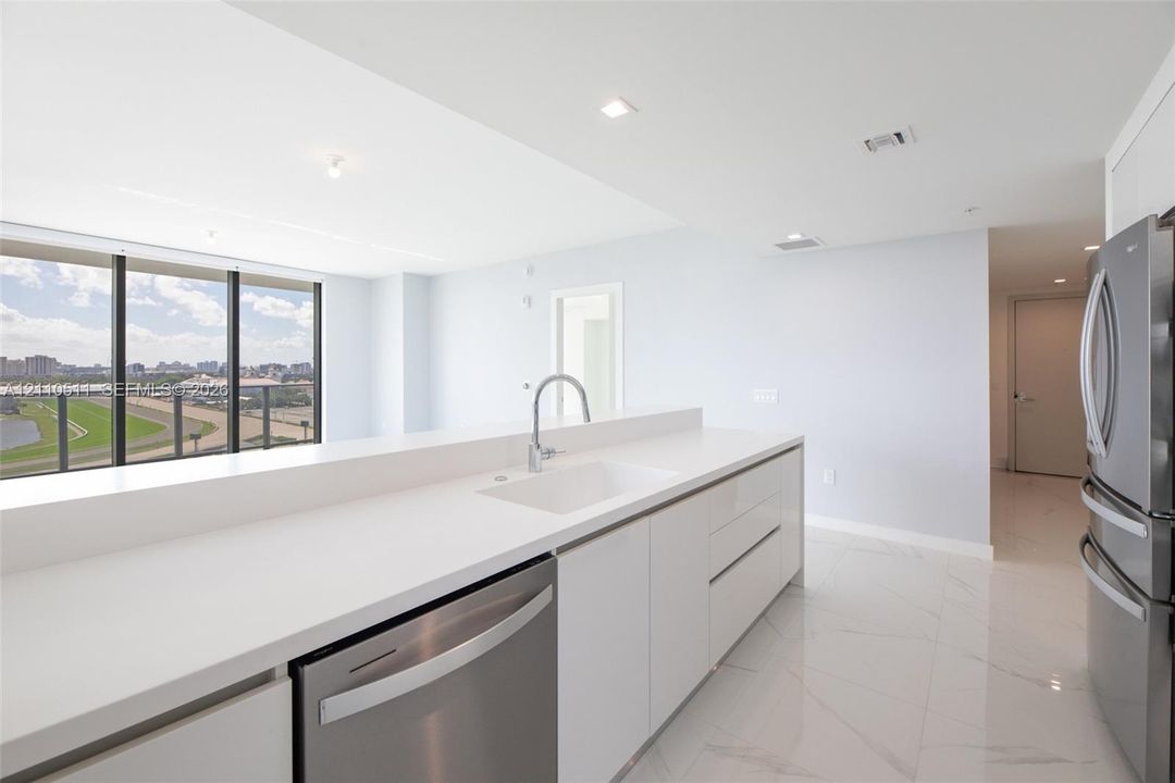 Kitchen featuring high-gloss white cabinetry, white stone countertops, stainless steel appliances, and large-format tile flooring