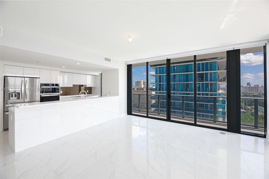 Open-concept kitchen featuring high-gloss cabinetry, stainless steel appliances, and a breakfast bar, highlighted by large-format flooring and floor-to-ceiling glass sliding doors