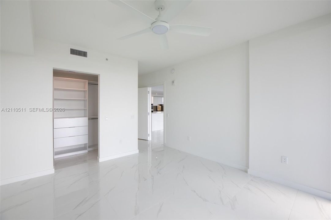 Interior space featuring white stone-finish tile flooring, ceiling fan with integrated lighting, and walk-in closet with built-in shelving and drawer units
