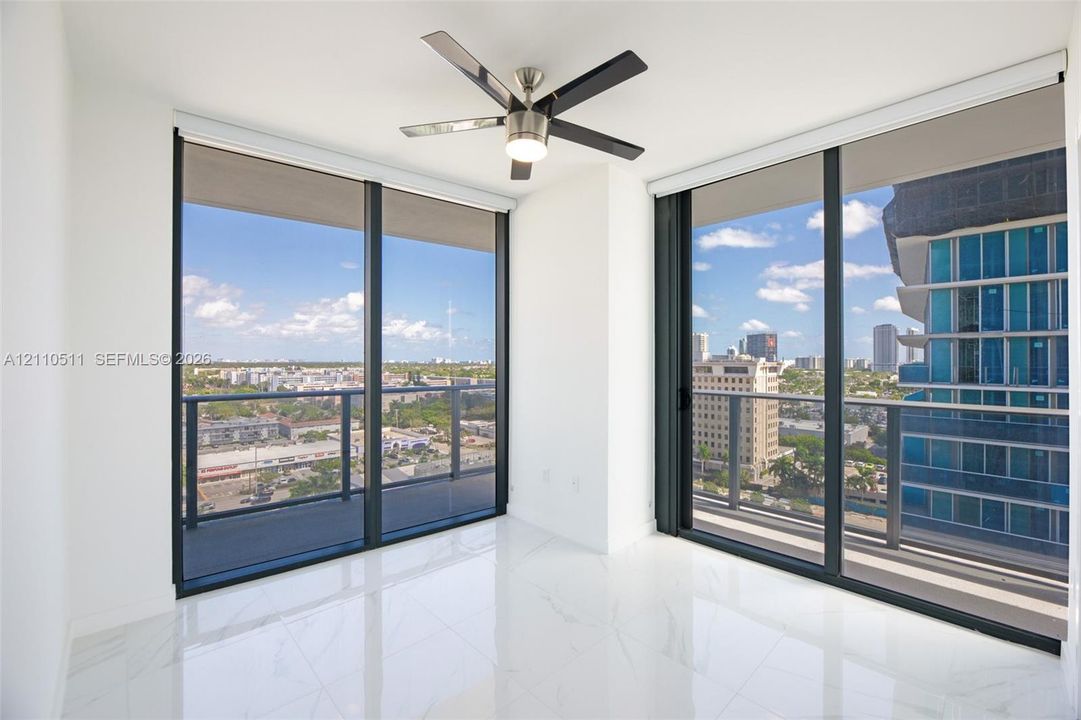 Third bedroom, floor-to-ceiling windows, polished stone-finish flooring, integrated balcony access, and a multi-blade ceiling fan with light fixture