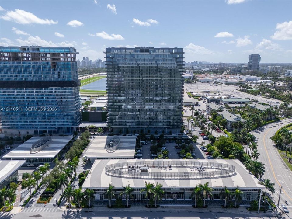 Aerial perspective of high-rise glass-facade towers featuring structured parking facilities with geometric roof patterns and integrated palm tree landscaping