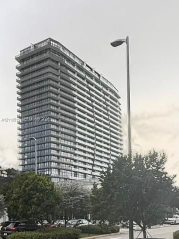 High-rise residential building featuring a glass facade, multiple levels of balconies with glass railings, and a tiered architectural design