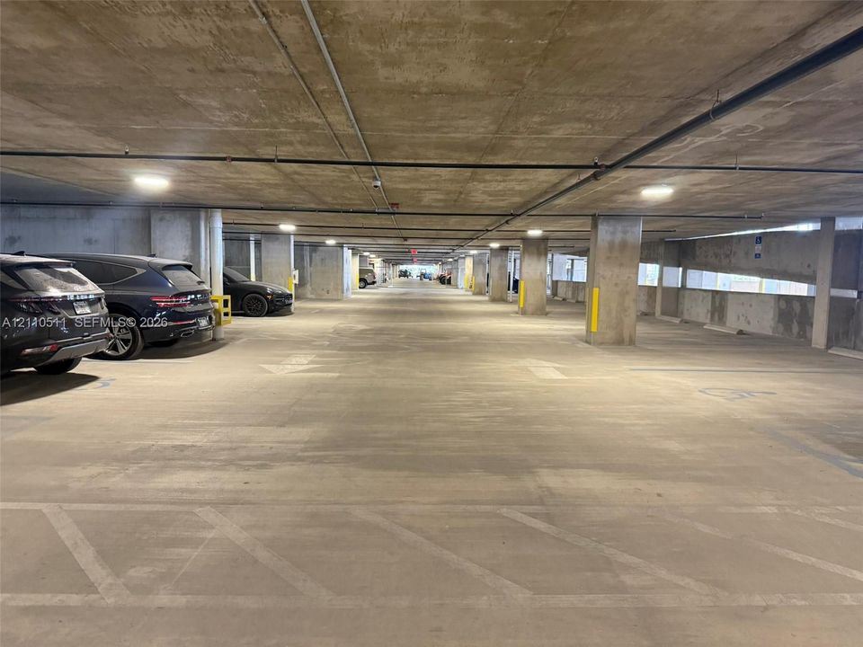 Covered parking garage featuring reinforced concrete construction, support pillars, overhead lighting, and designated parking stalls