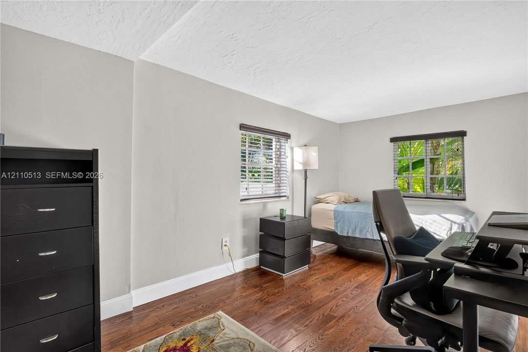 Room interior featuring wood-finish flooring, two windows with horizontal blinds, and neutral wall tones