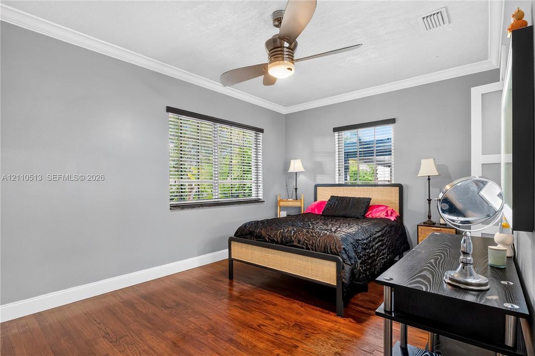 Room featuring wood-finish flooring, crown molding, dual windows with horizontal blinds, and a ceiling fan with integrated lighting