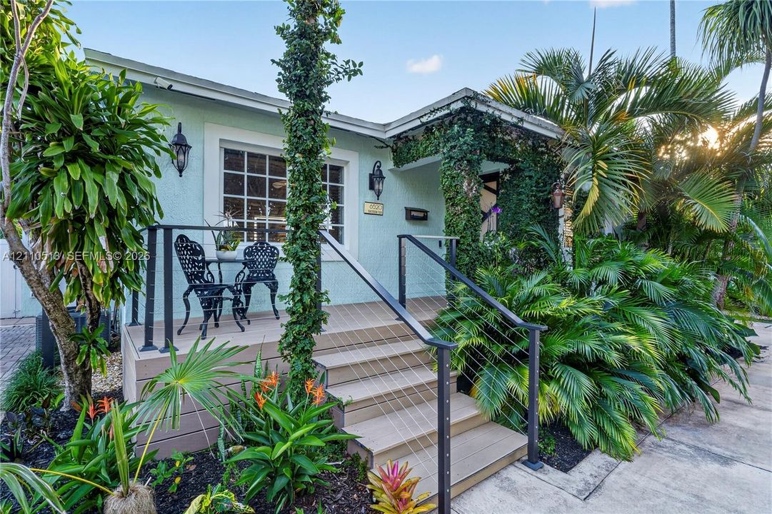 Exterior featuring light-colored stucco siding, raised composite decking, metal cable railings, and established landscaping