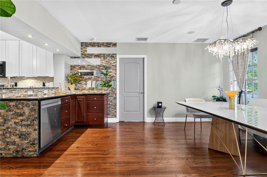 Kitchen featuring a stone-clad breakfast bar, dark wood cabinetry, white upper cabinets, wood-finish flooring, and a crystal chandelier