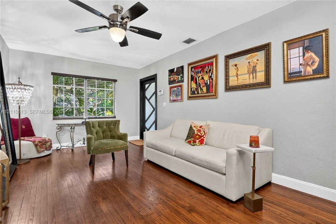 Living area featuring wood-finish flooring, a multi-blade ceiling fan with integrated lighting, and a front entry door with a geometric pane design