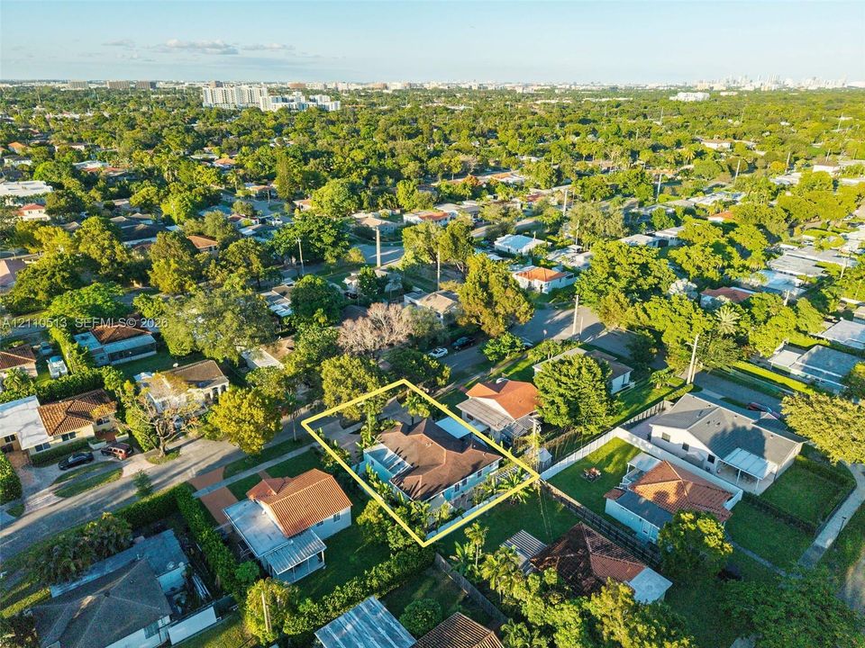 Aerial perspective of a residential property featuring a pitched roofline, paved driveway, enclosed backyard, and mature landscaping