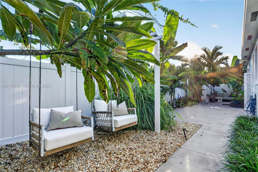 Private rear outdoor space featuring a paved patio, decorative gravel ground cover, a perimeter privacy fence, and mature tropical landscaping