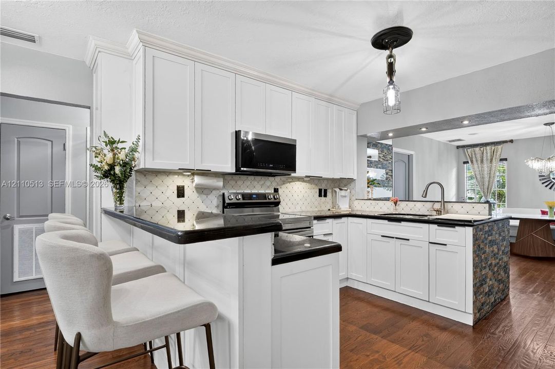 Kitchen featuring white shaker-style cabinetry, dark stone countertops, stainless steel appliances, decorative tiled backsplash, and wood-finish flooring