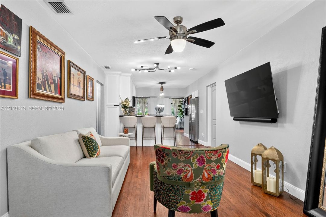 Wood-finish flooring, brushed nickel ceiling fan, multi-bulb modern chandelier, and kitchen breakfast bar with built-in cabinetry