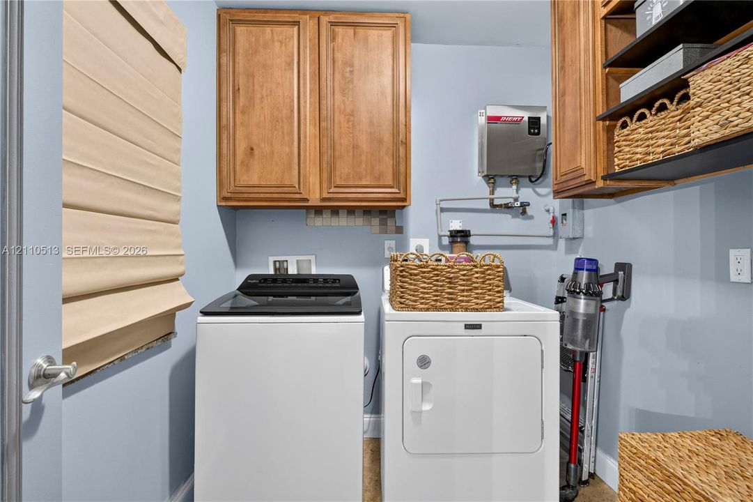 Laundry room featuring wood-finish wall-mounted cabinetry, integrated open shelving, and a tankless water heater