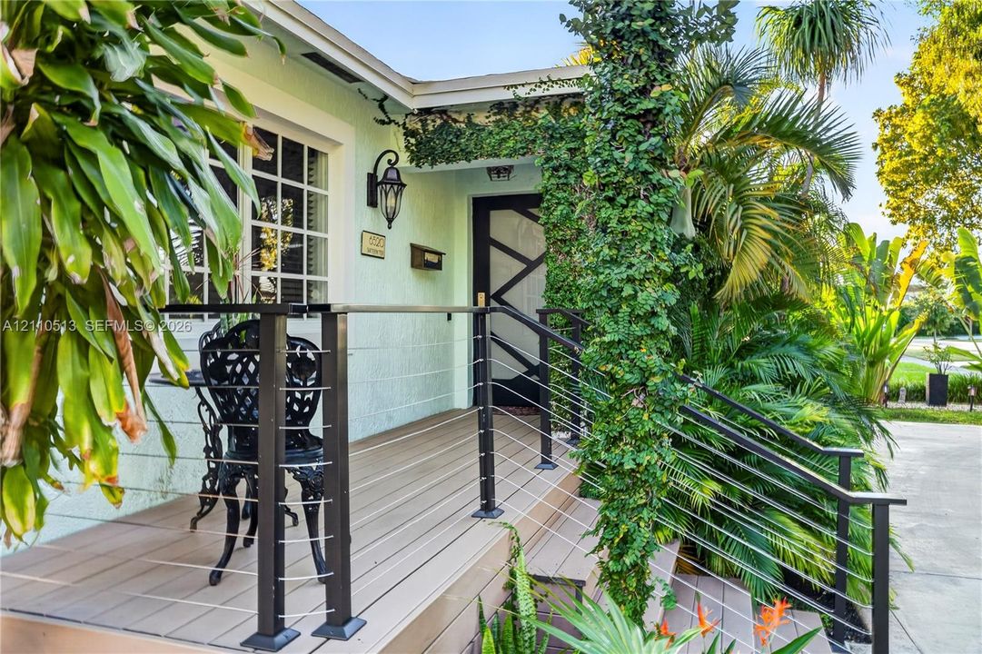Elevated porch featuring composite decking, black metal cable railings, custom geometric front door, and traditional wall-mounted lantern lighting
