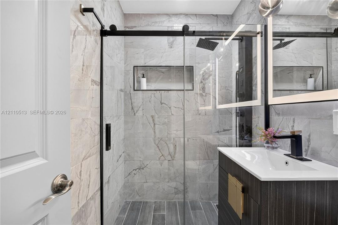 Walk-in shower with floor-to-ceiling large-format tile, glass sliding door, and recessed wall niche