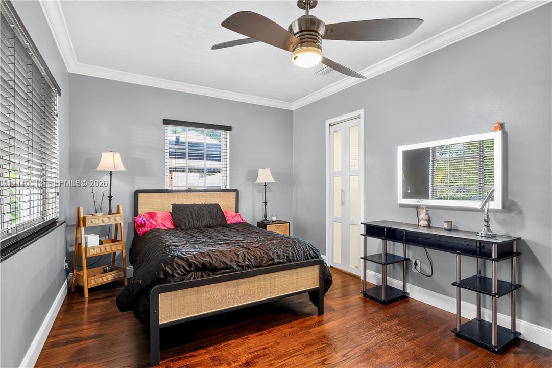 Bedroom featuring wood-finish flooring, crown molding, a multi-blade ceiling fan with integrated lighting, horizontal window blinds, and a multi-panel door