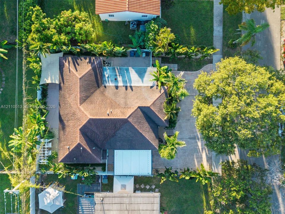 Aerial perspective featuring a multi-faceted shingle roof, concrete driveway, paved exterior patio, and mature landscaping