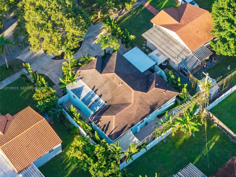 Aerial perspective of a property featuring a multi-pitched shingled roof, a paved driveway, and mature landscaping enclosed by white perimeter fencing