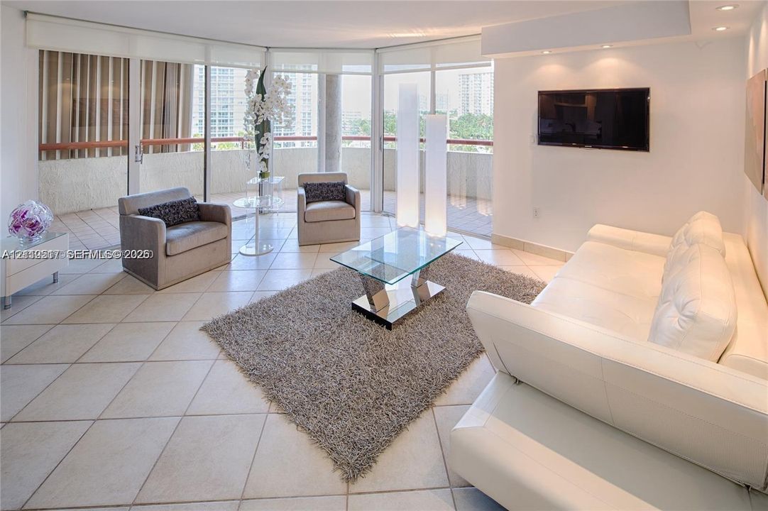 Expansive living area featuring light-toned tile flooring, recessed ceiling lighting, and floor-to-ceiling glass sliding doors providing access to a private balcony
