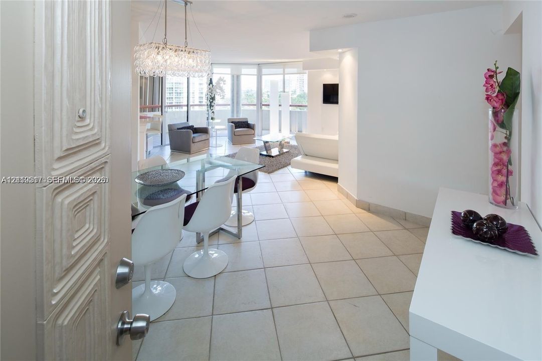 Large-format tile flooring, crystal-accented chandelier, and floor-to-ceiling glass paneling featuring balcony access