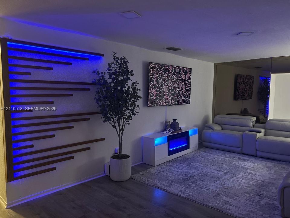 Custom wood-slat accent wall with integrated blue LED lighting, wood-finish flooring, and mirrored wall paneling