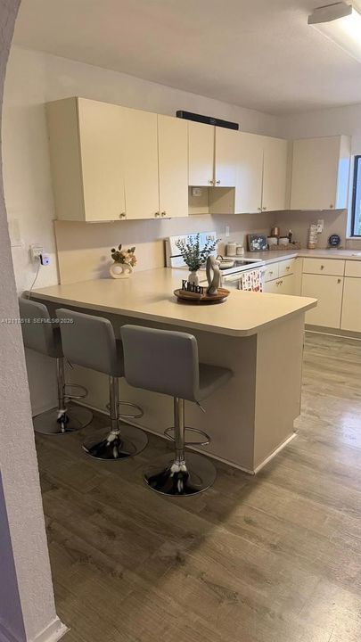Kitchen featuring solid-surface countertops, peninsula with breakfast bar, light-finish cabinetry, and wood-finish flooring