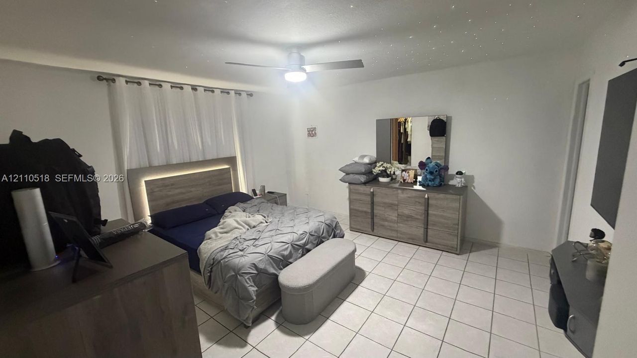 Spacious room featuring neutral tile flooring, a central ceiling fan with integrated lighting, and a textured ceiling finish