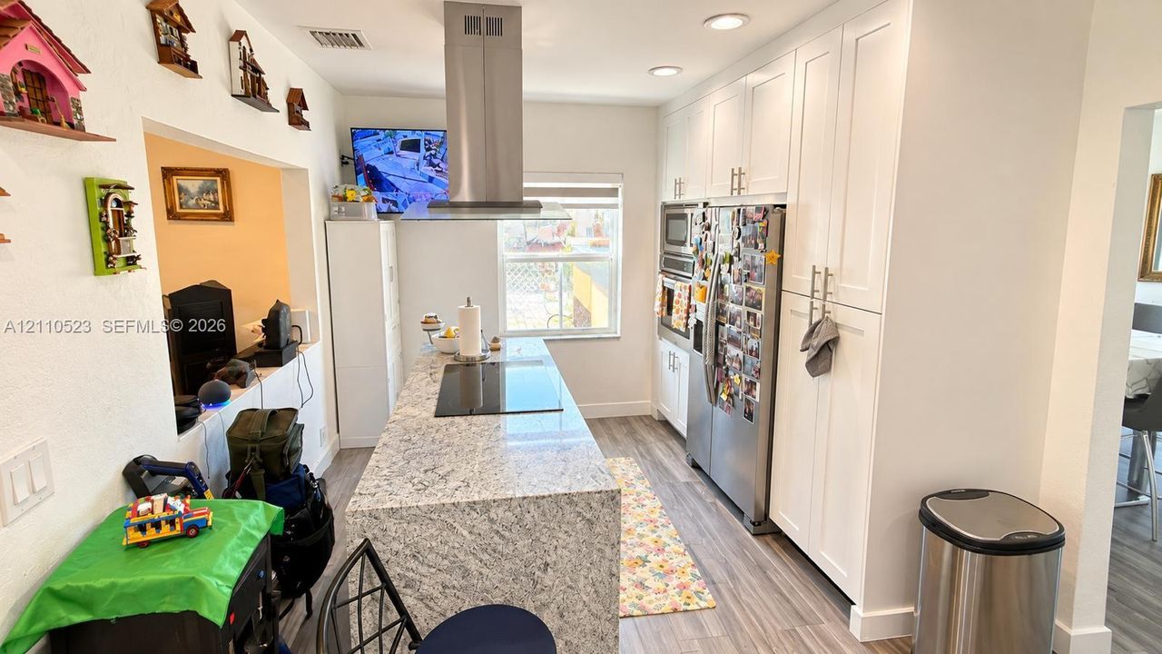 Kitchen featuring white cabinetry, stone-finish island countertop, stainless steel appliances, stainless steel chimney-style range hood, and wood-finish flooring