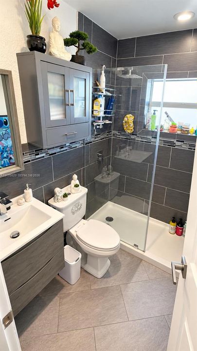 Bathroom featuring a floating vanity with a vessel sink, a walk-in shower with glass enclosure, floor-to-ceiling large-format tile surround, and built-in wall cabinetry
