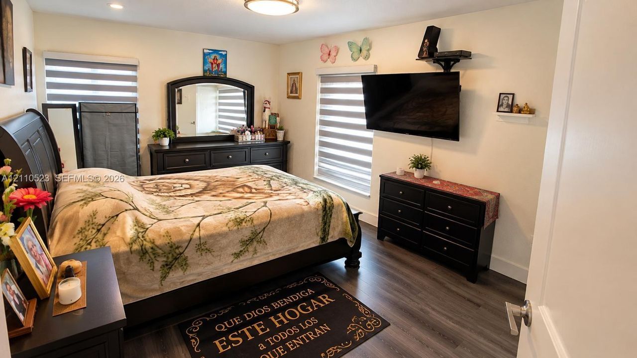Bedroom featuring wood-finish flooring, dual-tone roller shades, and a flush-mount ceiling light fixture
