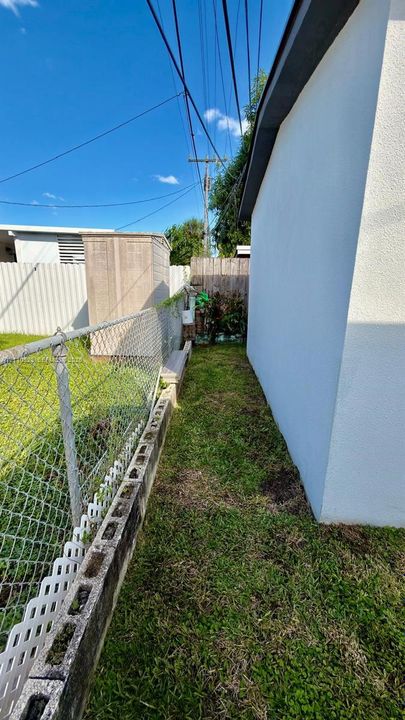 Exterior side yard featuring a chain-link fence, concrete block border, and lawn