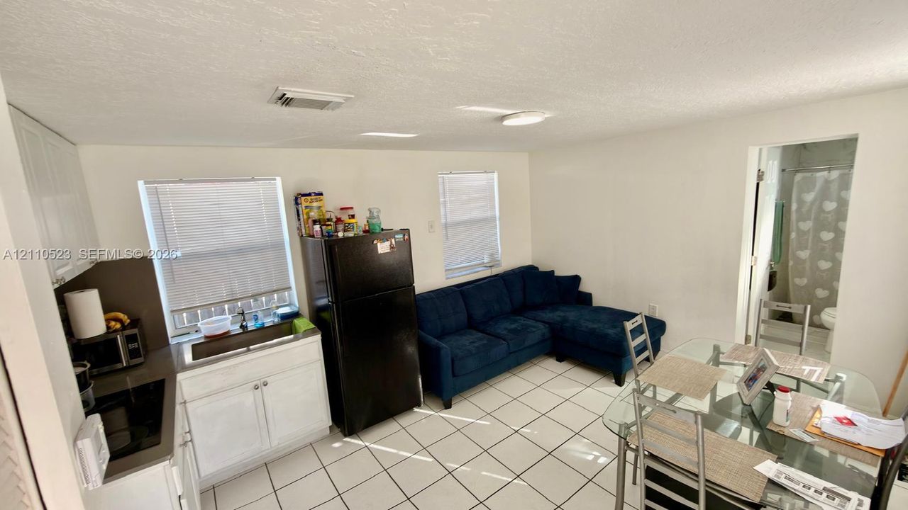 (Separate apartment) Kitchenette featuring white shaker-style cabinetry, a stainless steel sink with a chrome faucet, solid-surface countertops, and tiled flooring