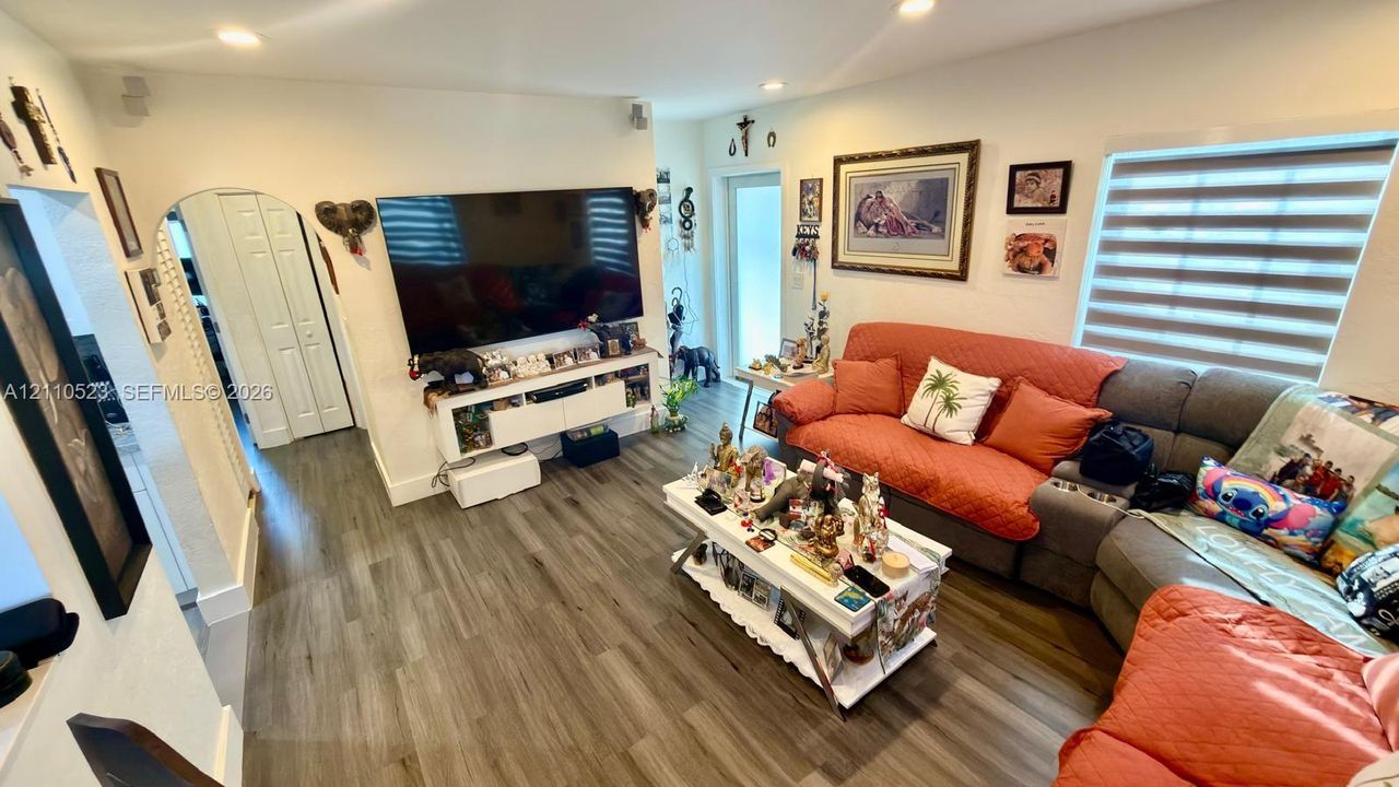 Living area featuring wood-finish flooring, recessed lighting, arched doorway, and large windows with horizontal blinds
