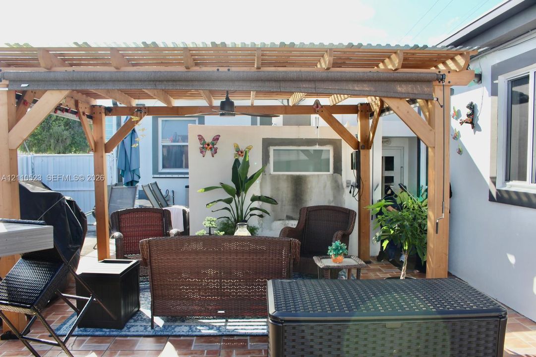 Covered outdoor living space featuring a timber-frame pergola, integrated ceiling fan, tiled patio flooring, and a built-in outdoor masonry fireplace