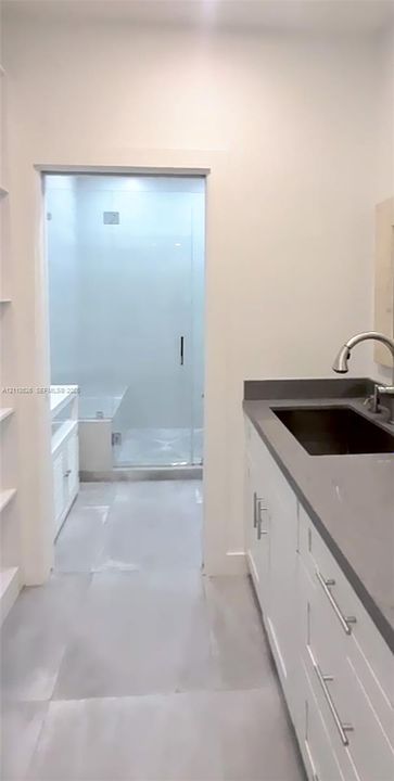 Bathroom vanity featuring white shaker-style cabinetry, a solid surface countertop, an undermount sink with a gooseneck faucet, and a glass-enclosed shower with tiled walls