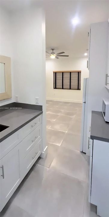 Kitchen featuring white shaker-style cabinetry, solid-surface countertops, large-format tile flooring, and integrated ceiling lighting