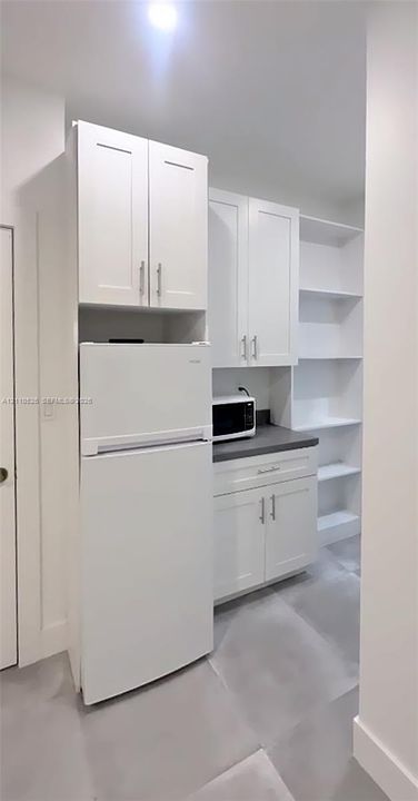 White cabinetry with brushed metal hardware, dark solid-surface countertop, and built-in open shelving