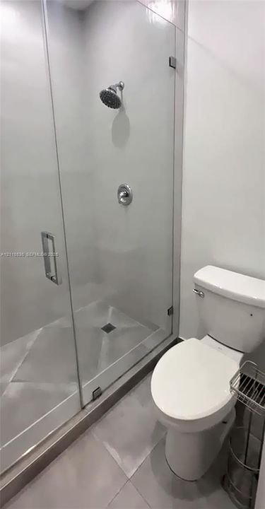 Glass-enclosed shower with polished chrome fixtures and tile flooring