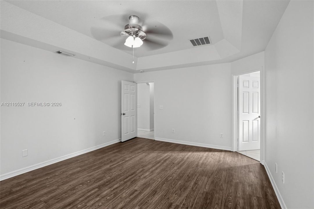 Tray ceiling featuring a central brushed-nickel ceiling fan with integrated lighting and wood-finish flooring