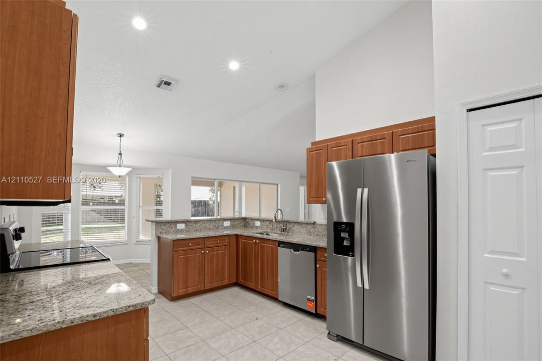 Kitchen featuring wood cabinetry, stone-finish countertops, stainless steel appliances, tile flooring, and vaulted ceilings