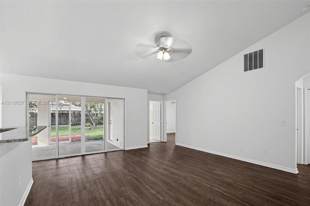 Open-concept living space featuring vaulted ceilings, wood-finish flooring, a ceiling fan with light fixture, and sliding glass doors