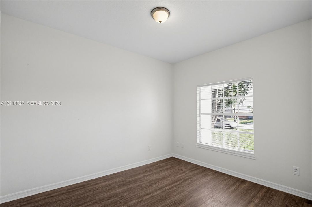 Room featuring neutral-toned walls, wood-finish flooring, a multi-pane window with integrated blinds, and a dome-style flush-mount ceiling light