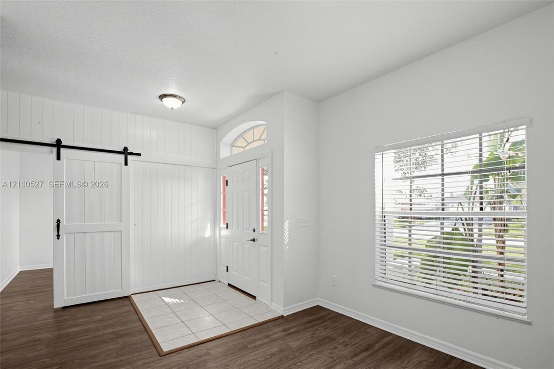 Entryway featuring vertical white wood-paneling, a sliding barn door, ceramic tile flooring, wood-finish flooring, and an arched transom window above the front door