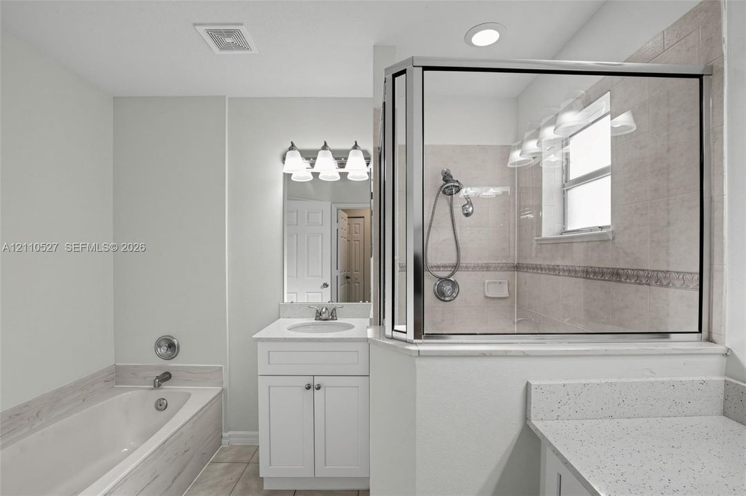 Bathroom featuring a glass-enclosed shower with tiled walls, a deep soaking tub with a tiled surround, white shaker-style cabinetry, and light-toned solid surface countertops