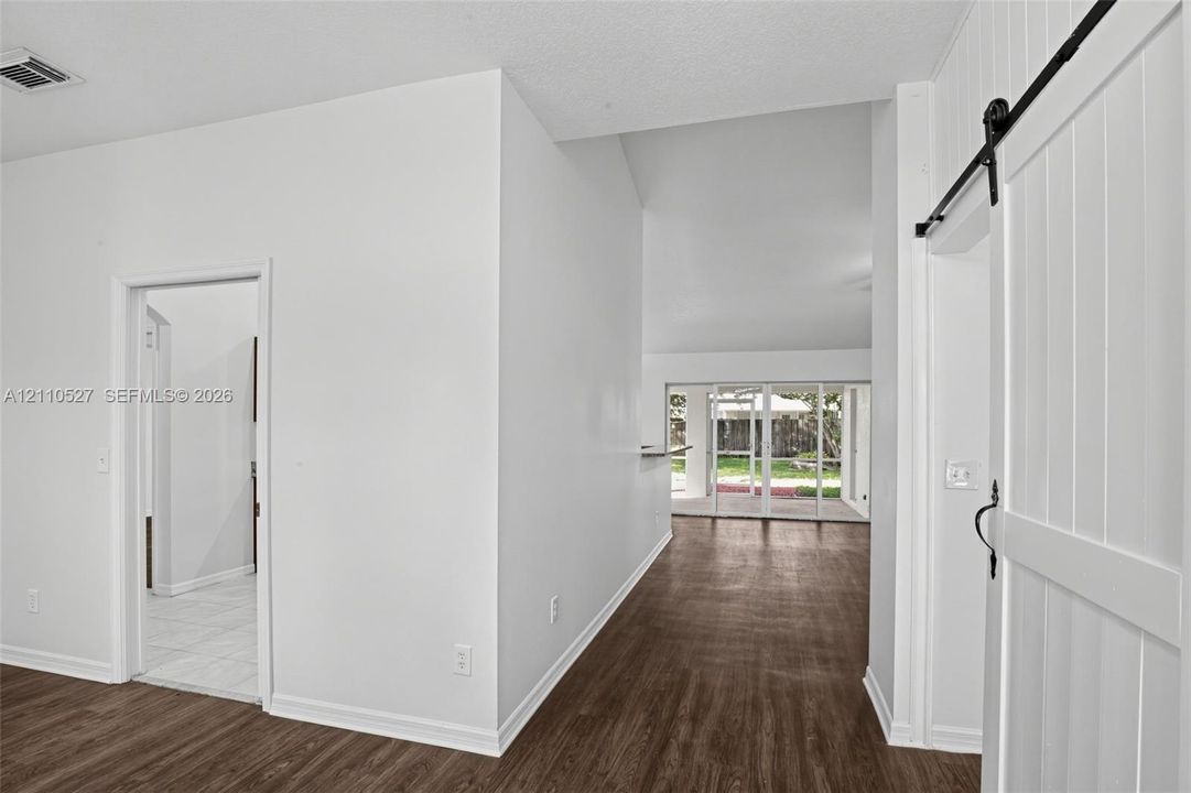 Interior featuring white vertical-plank sliding barn door, wood-finish flooring, vaulted ceilings, and multi-panel sliding glass doors