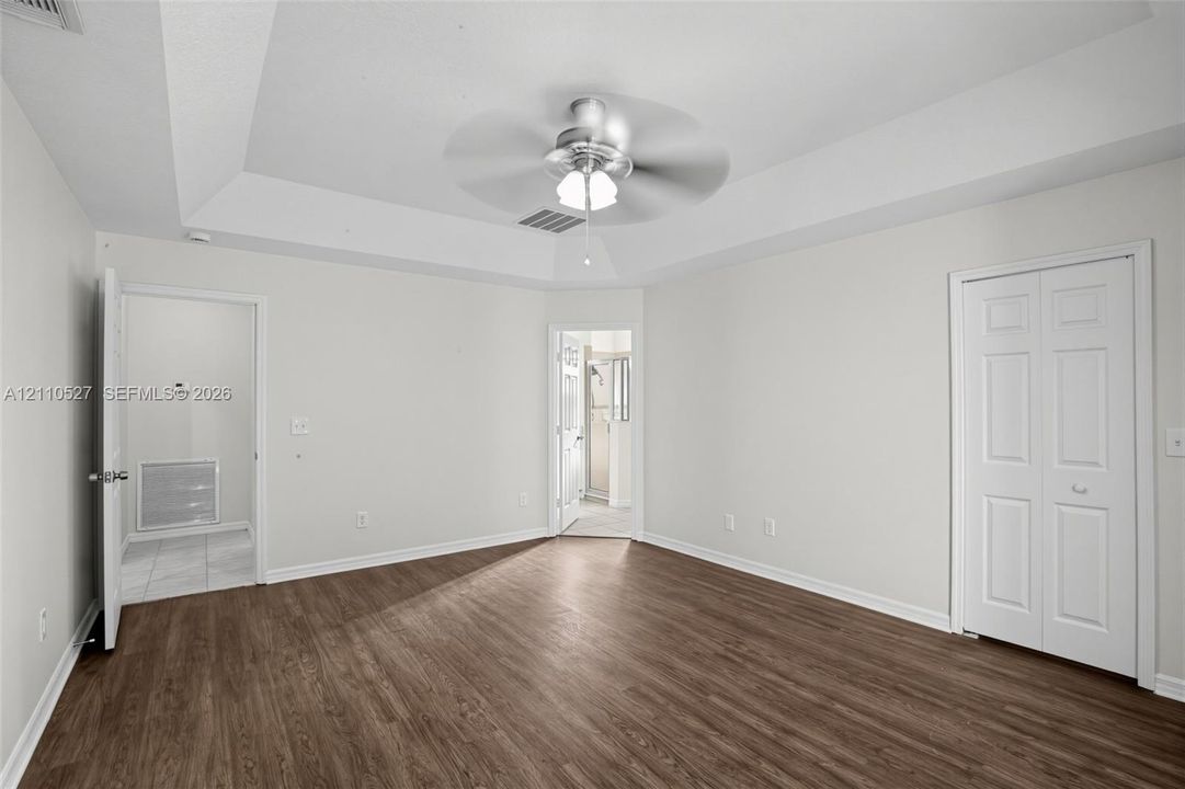 Tray ceiling featuring a central brushed-metal ceiling fan, wood-finish flooring, and white two-panel closet doors
