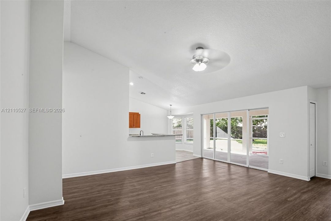Open living area featuring vaulted ceilings, wood-finish flooring, a ceiling fan, and sliding glass doors with exterior access
