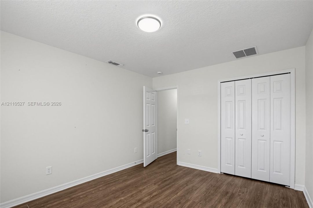 Room with neutral wall color, wood-finish flooring, white paneled interior door, and white bi-fold closet doors
