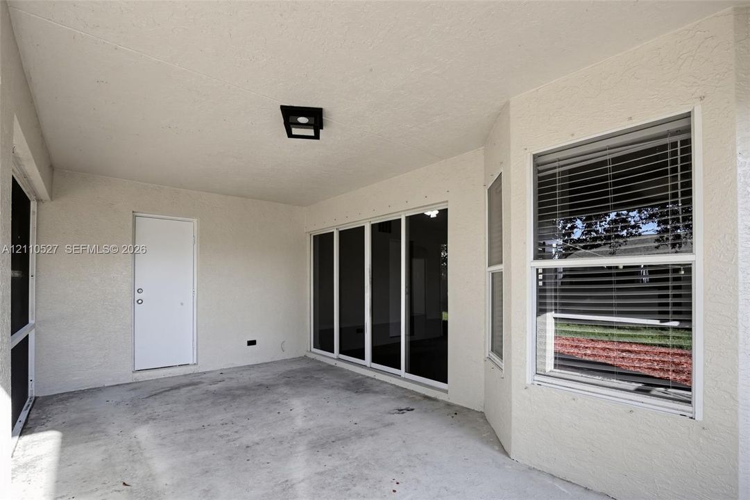 Covered patio featuring concrete flooring, multi-panel sliding glass doors, a single-panel door, and a built-in flush-mount light fixture
