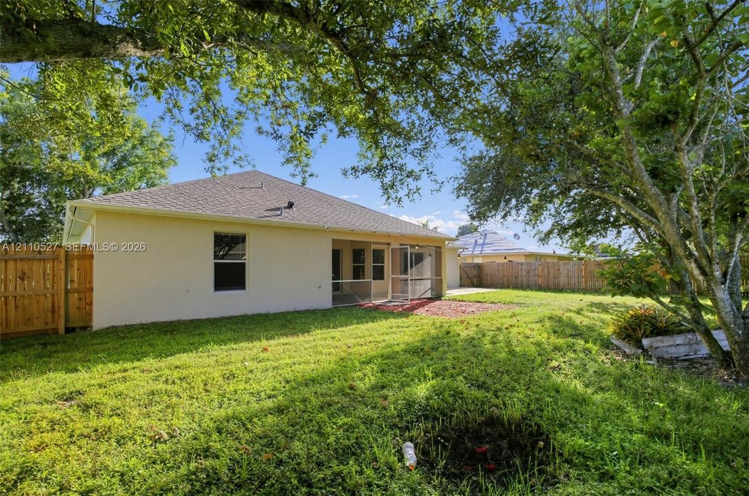 Rear exterior featuring stucco siding, a screened-in lanai, wood privacy fencing, and mature trees
